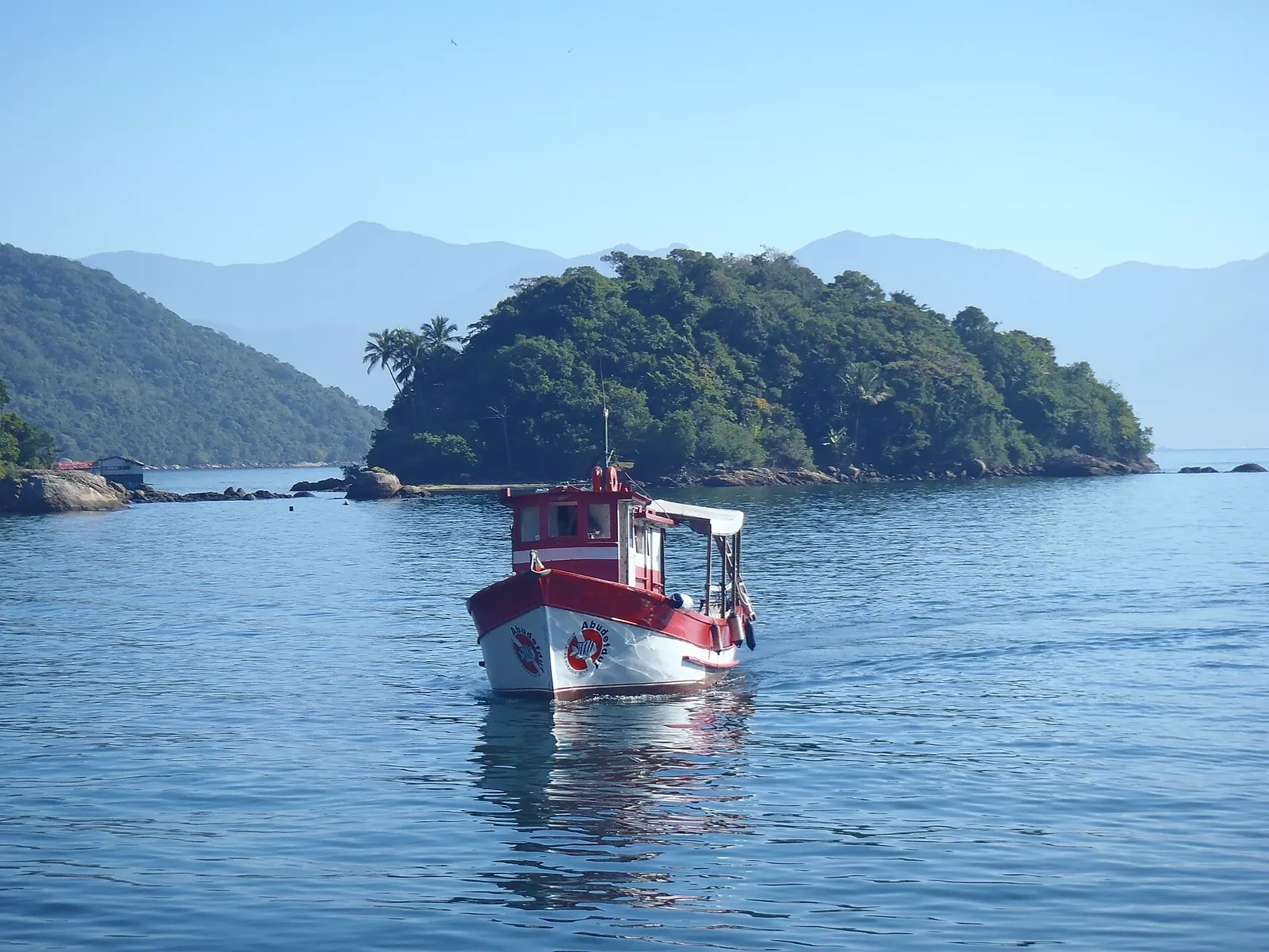 Barco de pesca vermelho e branco parado no mar calmo da Ilha Grande